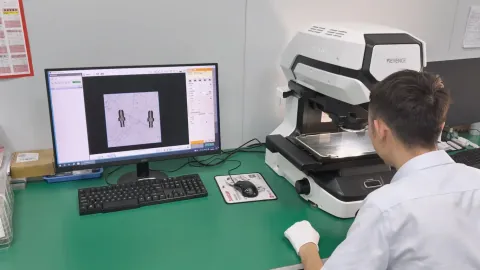 OUJI operator inspecting small turned parts on KEYENCE optical equipment; process photograph